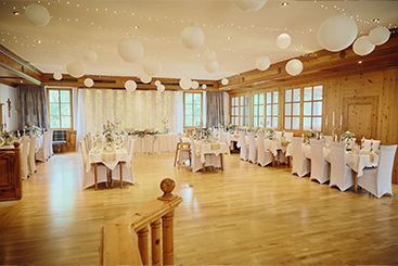 Eine Hochzeitsfeier in einem großen Raum mit weißen Tischdecken und weißen Luftballons.