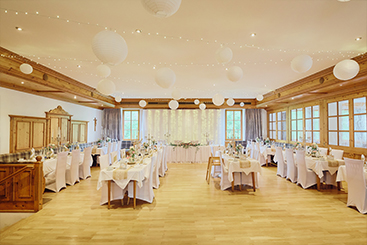 Ein geräumiger Raum mit weißen Tischen und Stühlen, perfekt für Hochzeitsfeiern.