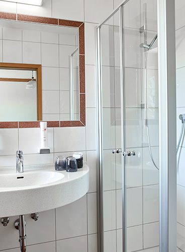 Impressionen eines Badezimmers mit Dusche, Waschbecken und Spiegel.
